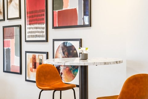 a dining room with orange chairs and a marble table and pictures on the wall