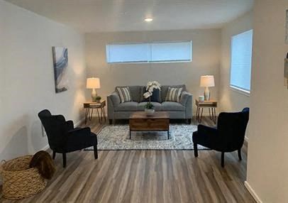 A living room with a grey couch, two black chairs, and a wooden floor.