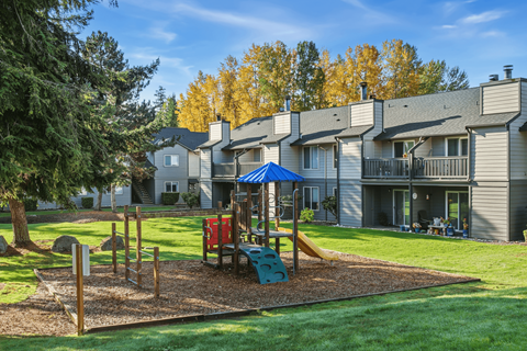 A playground with a red slide and a blue canopy is in the foreground of a residential area with houses and trees.