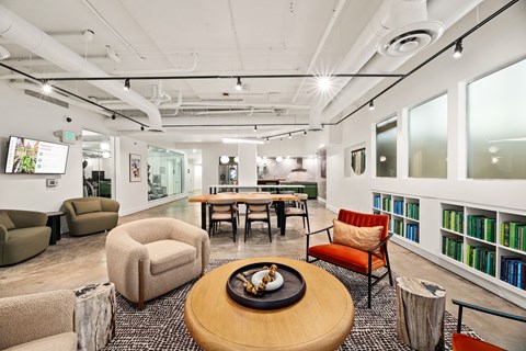 A modern office space with a wooden table in the center and a bookshelf filled with books on the right.