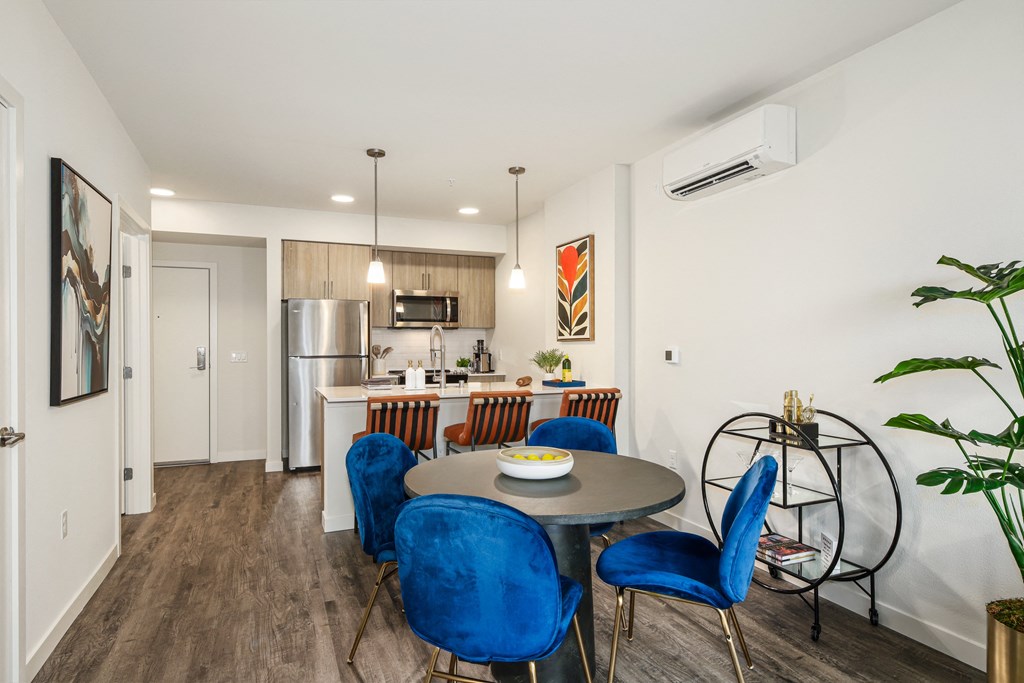 a dining area with a table and chairs and a kitchen with a refrigerator