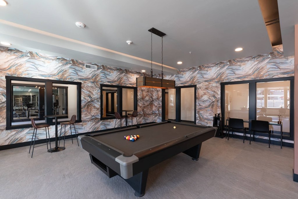 a pool table in a billiards room with windows and a bar