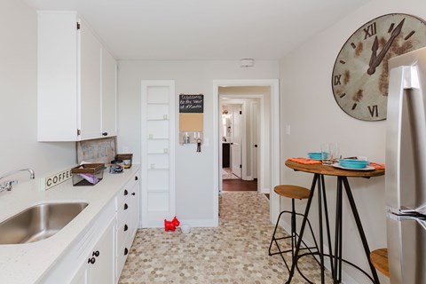 A kitchen with a clock on the wall and a refrigerator on the right.