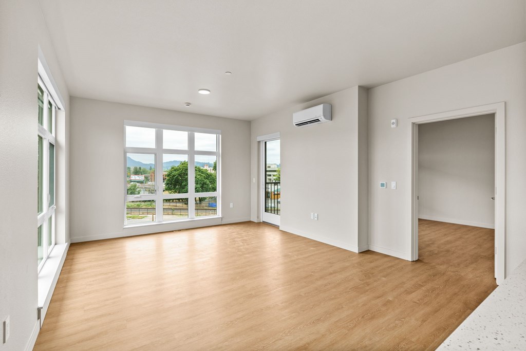 A spacious room with wooden floors and large windows overlooking a green landscape.