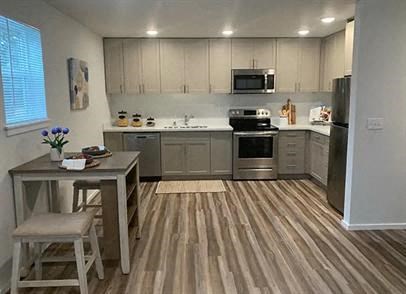 A kitchen with wooden floors and a table with a vase of flowers on it.