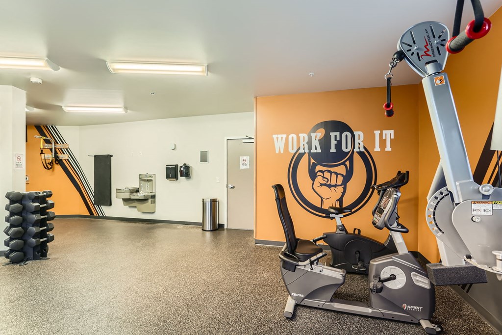 A gym with a row of treadmills and a wall with a fist graphic and the words "work for it".