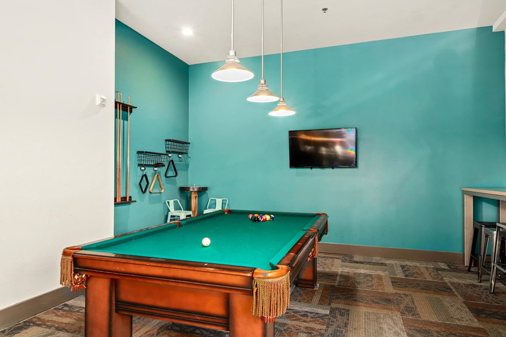 A pool table in a room with a television mounted on the wall.