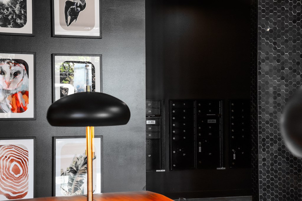 a black wall with pictures and a black chair with a gold lamp