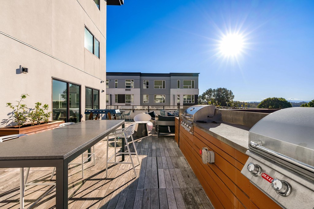 A sunny day at a rooftop patio with a grill and seating area.