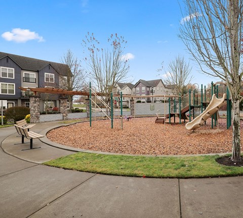 A playground with a slide, swings, and a bench in front of a building.