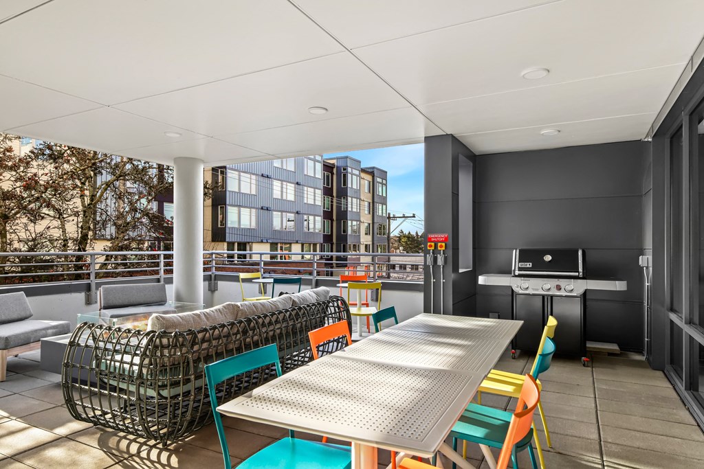 A modern outdoor dining area with a long table surrounded by colorful chairs.