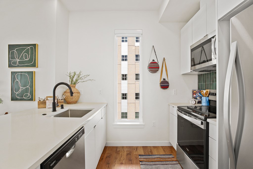 A kitchen with white cabinets and a window with a view of a building outside.