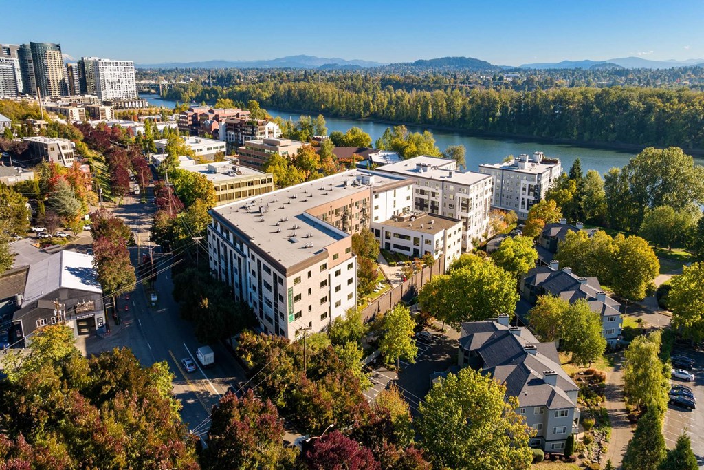 A large building sits in the middle of a residential area with a river and mountains in the background.