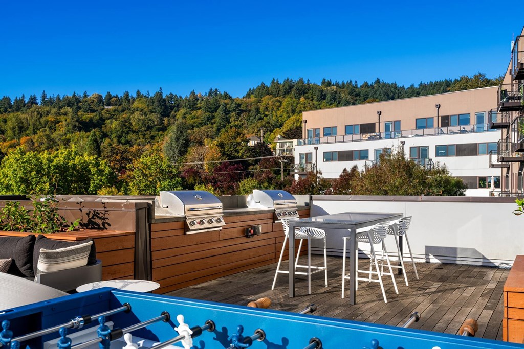 A blue hot tub sits on a wooden deck with a white table and chairs.