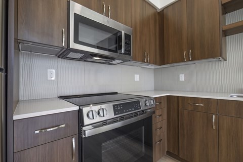 A modern kitchen with a stove, oven, microwave, and wooden cabinets.