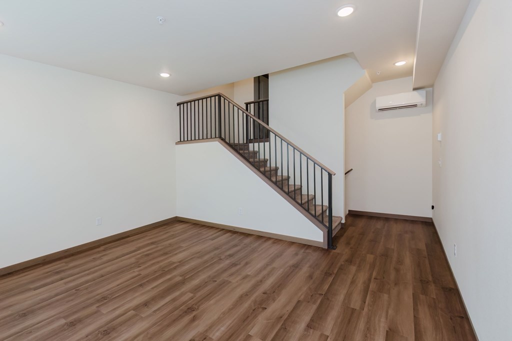 A room with a wooden floor and a staircase with a metal railing.