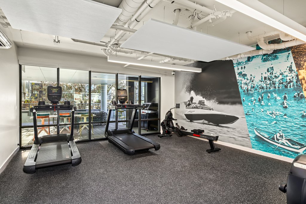 A gym with treadmills and a wall mural of people rowing.