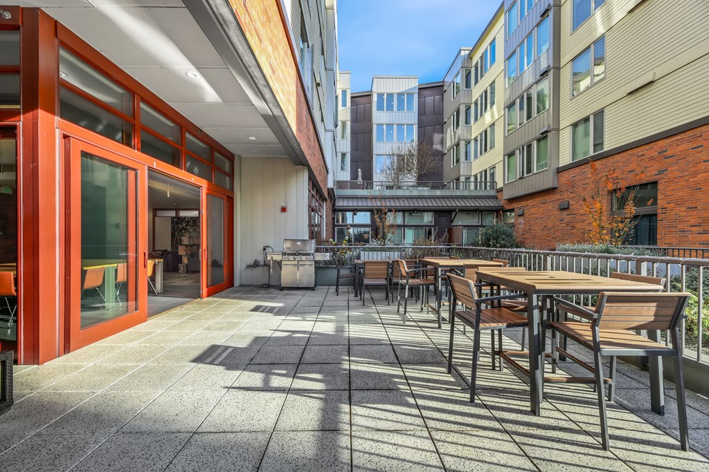 A patio with tables and chairs is surrounded by buildings.