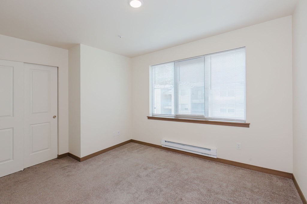 A room with a carpeted floor, a window with blinds, and a door.