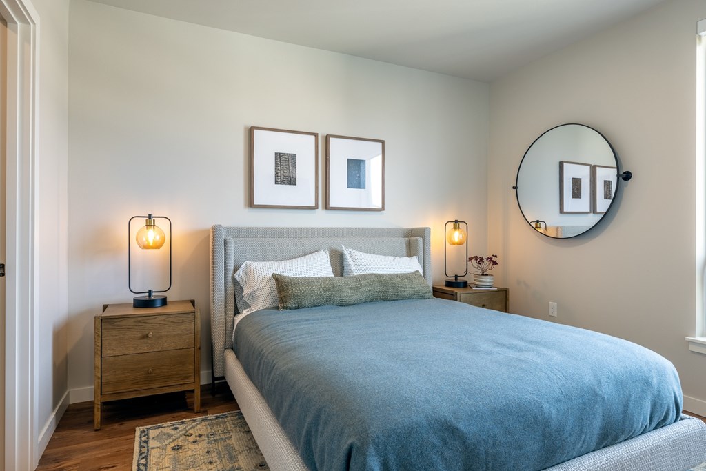 A bedroom with a bed, nightstands, and a round mirror on the wall.