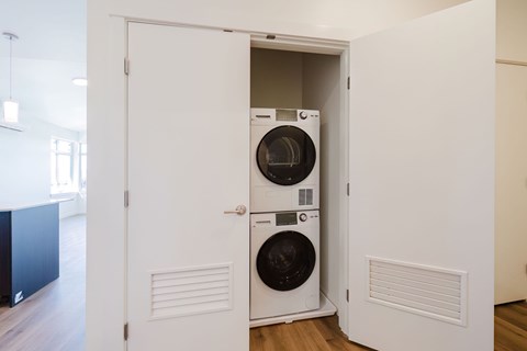 A white door is open to reveal a black washing machine and dryer.