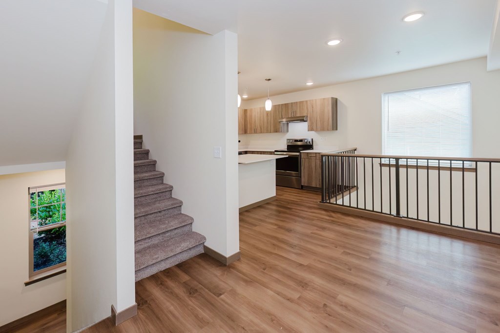 A staircase with a wooden handrail leads to a kitchen area.