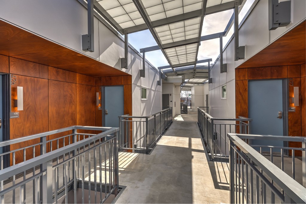 the building has a long corridor with metal railing and wooden doors