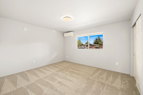 A room with a carpeted floor and a window showing a residential area outside.