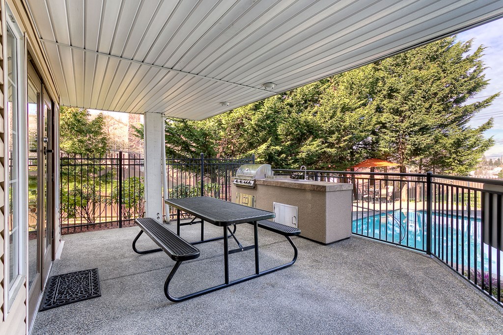 a patio with a grill and a table and a swimming pool