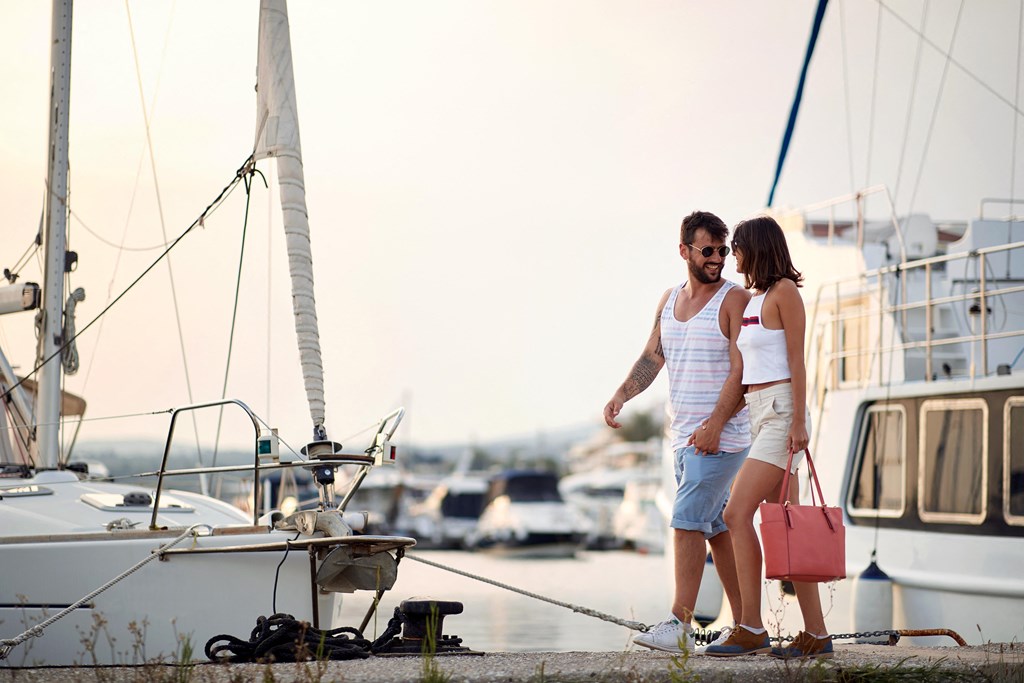 a couple standing on a dock with a boat in the background