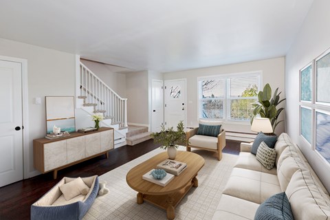 A living room with a white couch, a wooden coffee table, and a staircase.