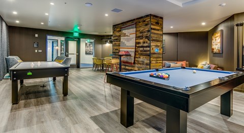A pool table in a room with a wooden floor and a green exit sign.