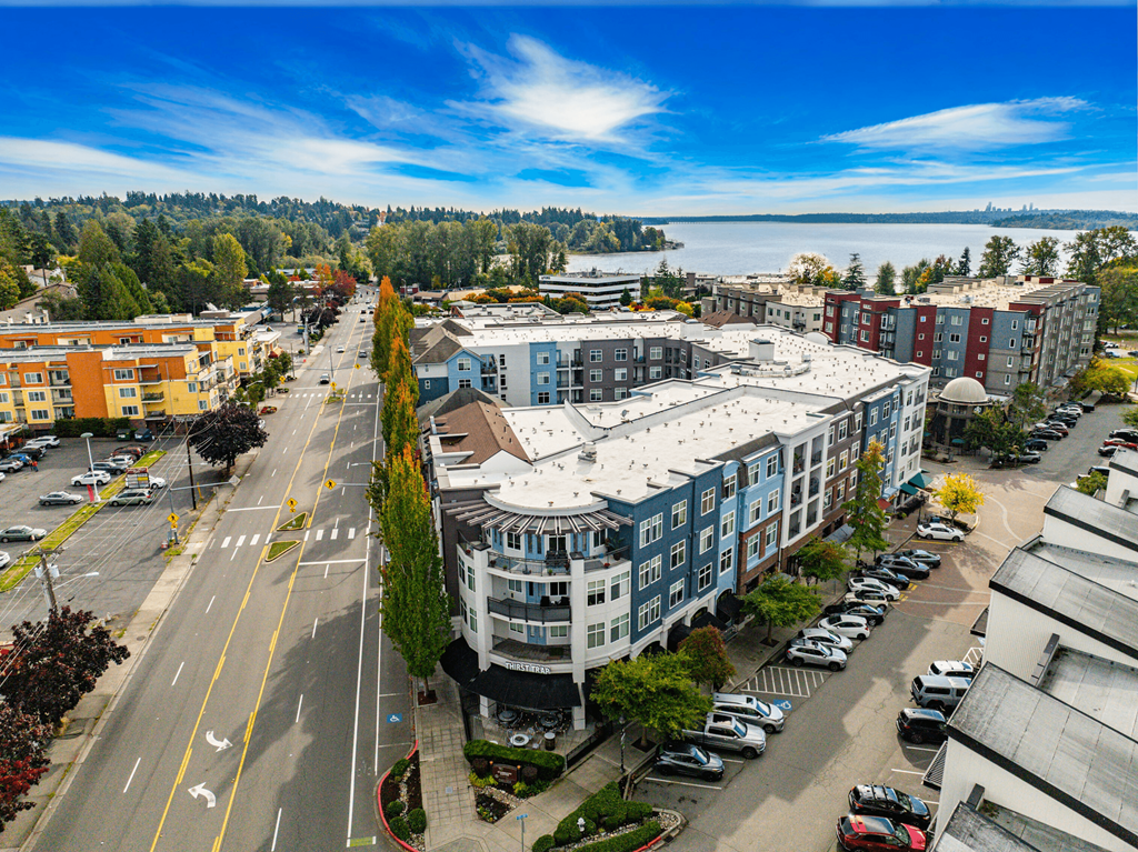 A street view of a residential area with apartment buildings and cars parked on the side of the road.