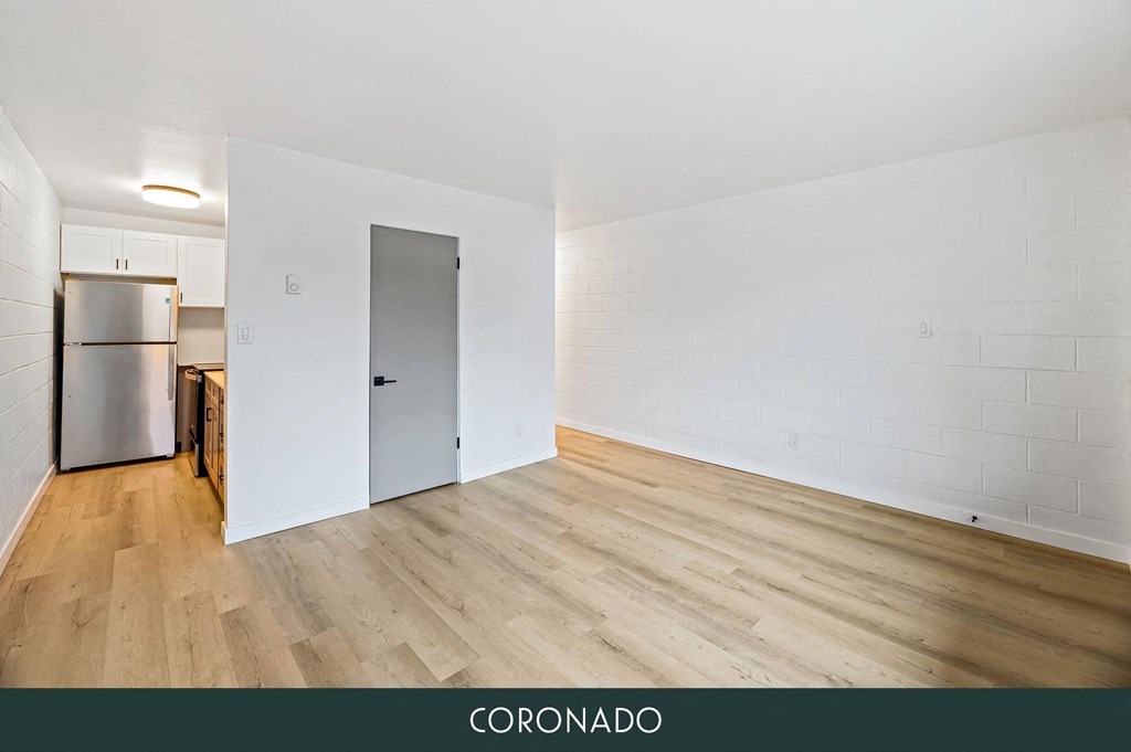the living room and kitchen of an apartment with white walls and wood floors