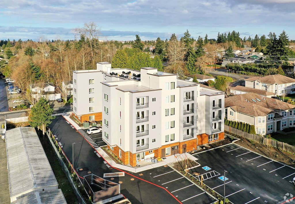 an aerial view of an apartment building with a parking lot and trees in the background