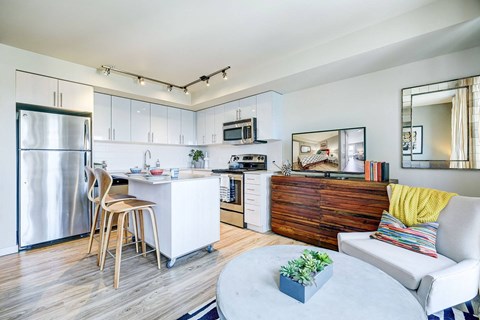 A modern kitchen with a white fridge, a white dining table with chairs, a white sofa with a yellow pillow, and a wooden cabinet.