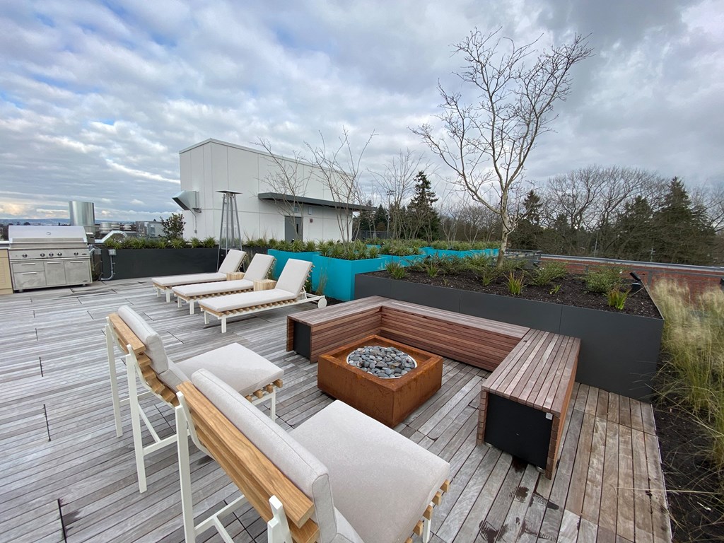 A rooftop patio with white chairs and a fire pit.