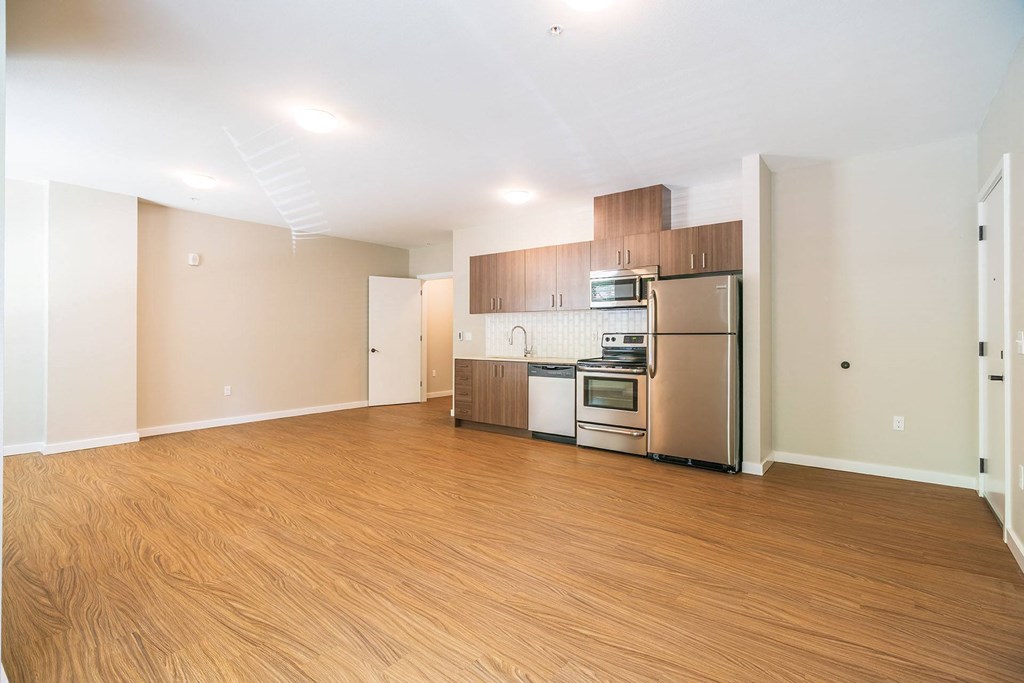 an empty living room with a kitchen with stainless steel appliances