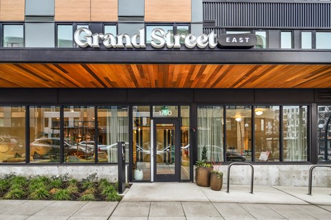 The Grand Street East building has a glass entrance and a wooden awning.