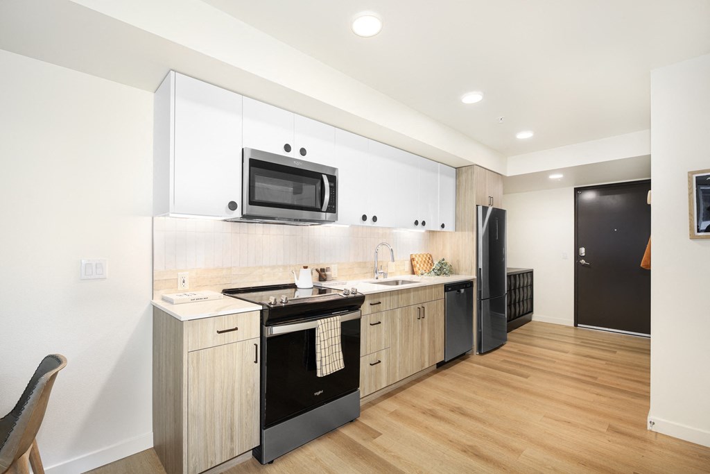 A modern kitchen with wooden floors and a black refrigerator.