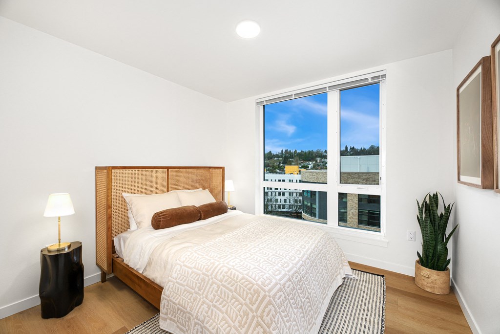 A bedroom with a large bed, a window with a view, and a plant.