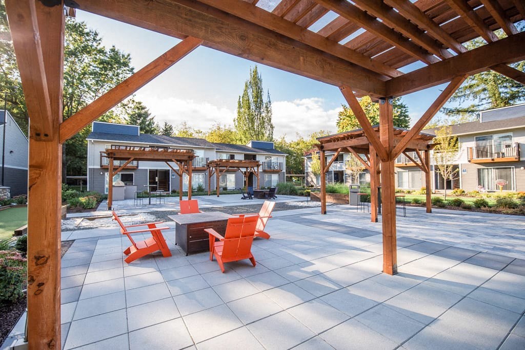 A wooden pergola over a patio with orange chairs and a table.