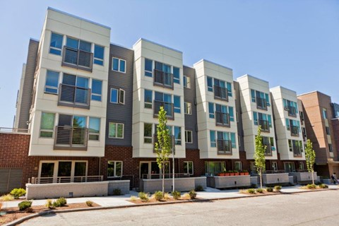 A row of modern apartment buildings with balconies and trees in front.