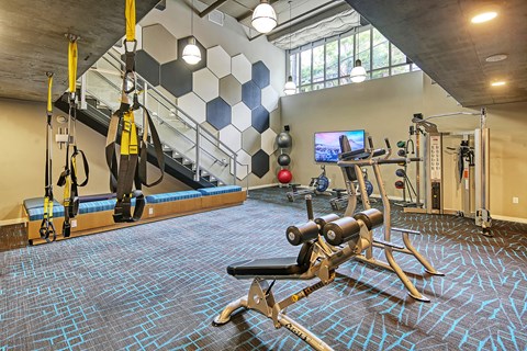 A gym with a variety of equipment including a rowing machine, a bench press, and a television.