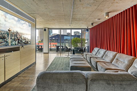 A long row of grey couches are lined up in a room with a large mural on the wall.