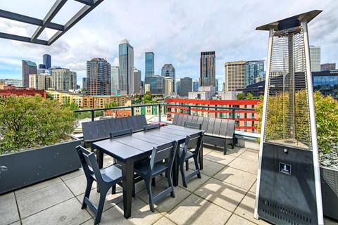 A table and chairs are set up on a rooftop terrace with a city skyline in the background.