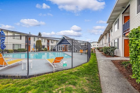 a fenced in swimming pool with orange lounge chairs and a building in the background