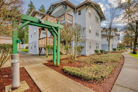 A green archway leads to a white building with a grey roof.