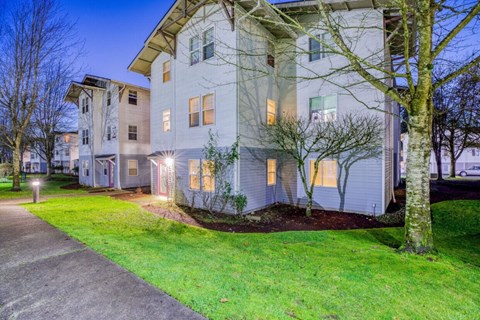 A modern apartment building with a well-maintained lawn and trees.