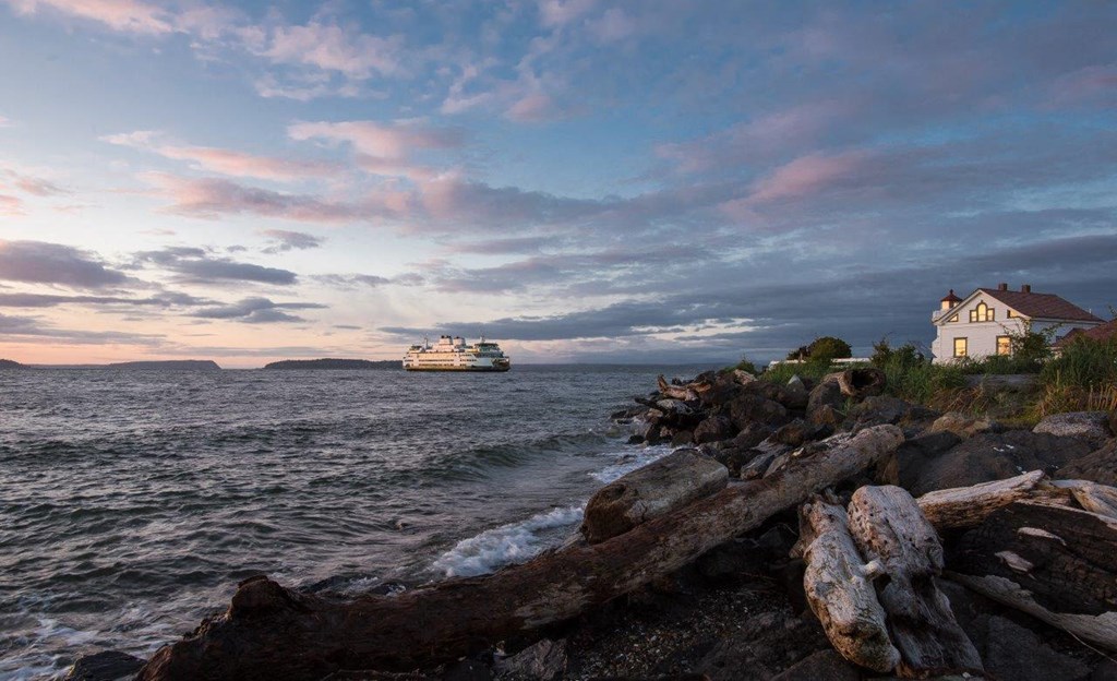 a cruise ship on the water near a shoreline with rocks and a lighthouse